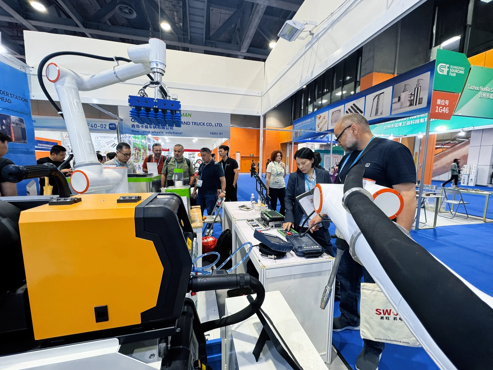 Visitors exploring a robotics exhibition booth with robot arms, a vacuum gripper and control equipment