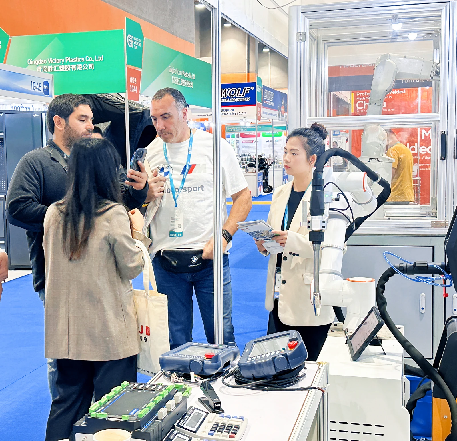 Visitors and team members discussing robotic equipment beside a robot arm and teach pendants