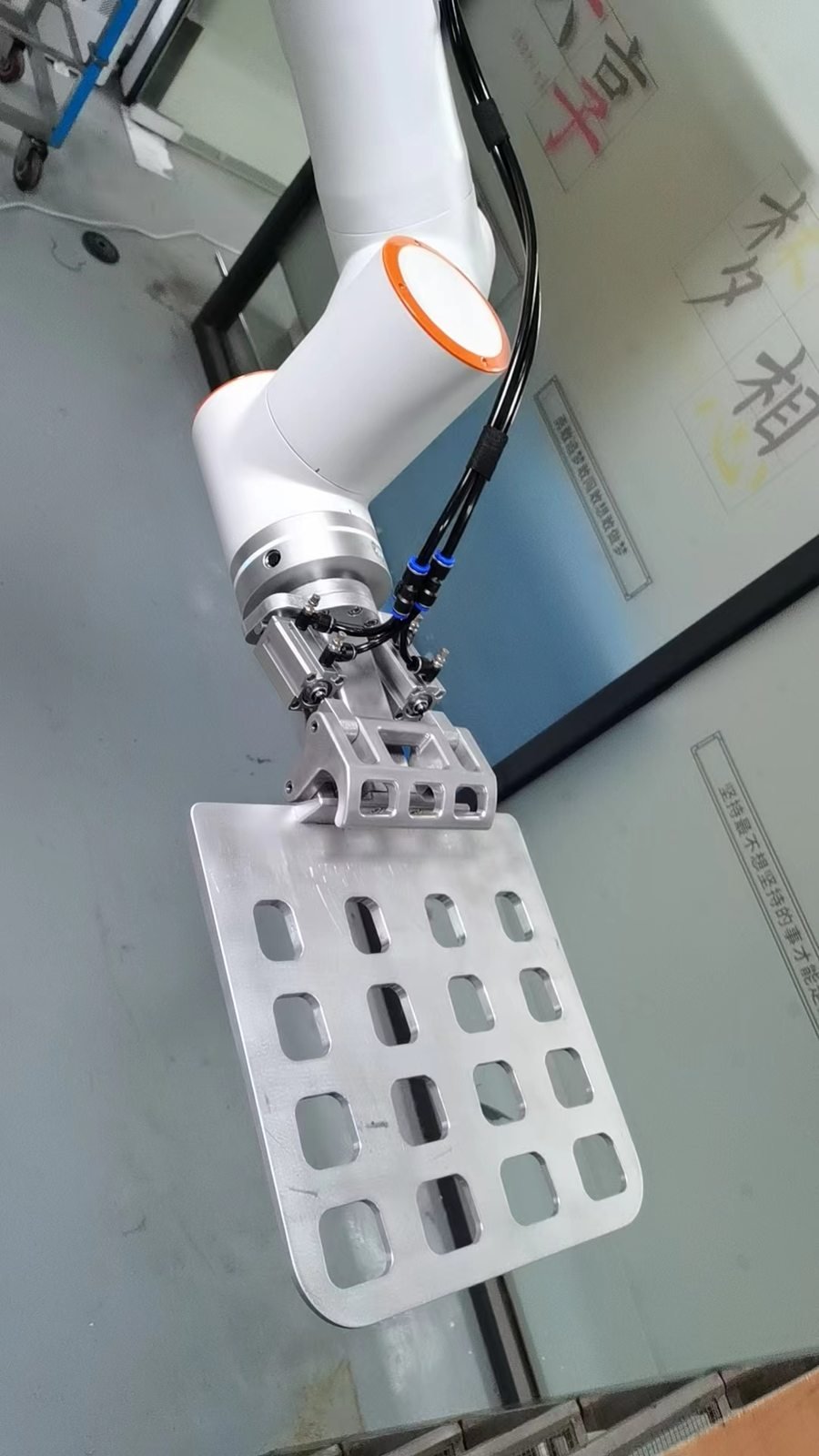 Robot end effector gripping a flat metal plate in a workshop